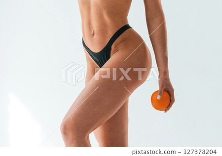 Orange fruit in hand, close up view. Young caucasian woman with athletic body shape is indoors at daytime Orange fruit in hand, close up view. Young caucasian woman with athletic body shape is indoors at daytime 127378204