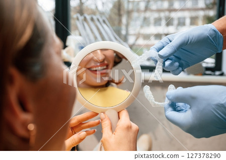 Using mirror to look at aligner on teeth. Woman in the stomatology clinic, visiting dentist 127378290