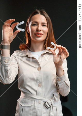 Standing and posing. Young woman is holding aligners 127378313