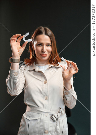 Against black background. Young woman is standing and holding aligner Against black background. Young woman is standing and holding aligner 127378317