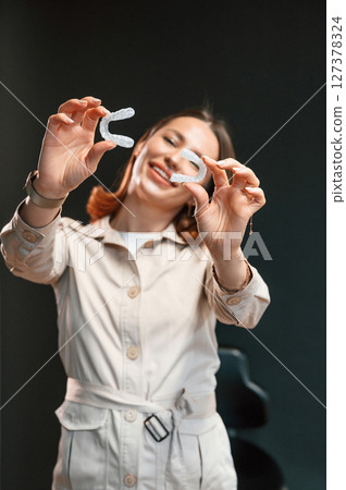 Holding two aligners. Young woman is standing against black background and holding Holding two aligners. Young woman is standing against black background and holding 127378324
