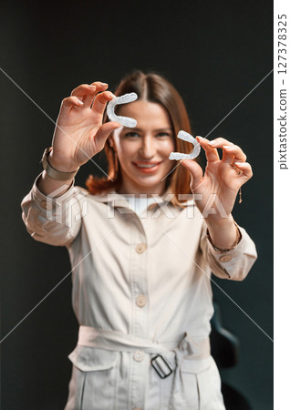 Holding two aligners. Young woman is standing against black background and holding Holding two aligners. Young woman is standing against black background and holding 127378325