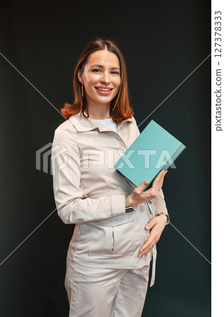Holding blue box. Young woman with aligner is standing against black background Holding blue box. Young woman with aligner is standing against black background 127378333