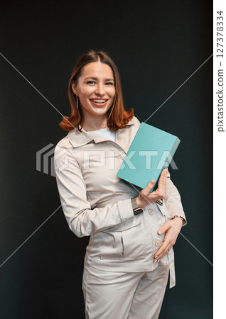 Holding blue box. Young woman with aligner is standing against black background 127378334