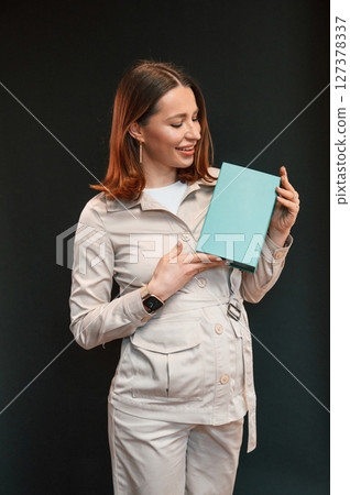 With blue box in hands. Young woman with aligner is standing against black background With blue box in hands. Young woman with aligner is standing against black background 127378337