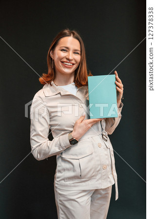 With blue box in hands. Young woman with aligner is standing against black background With blue box in hands. Young woman with aligner is standing against black background 127378338