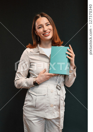 With blue box in hands. Young woman with aligner is standing against black background With blue box in hands. Young woman with aligner is standing against black background 127378340