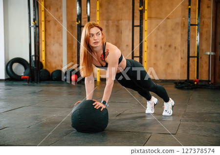 Doing push ups by using soft ball. Beautiful strong woman is in the gym 127378574