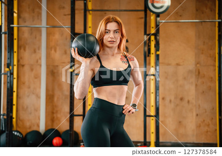 Holding ball. Beautiful strong woman is in the gym 127378584