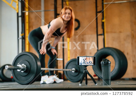 With barbell. Shooting video by smartphone. Beautiful strong woman is in the gym 127378592