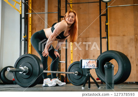 With barbell. Shooting video by smartphone. Beautiful strong woman is in the gym 127378593