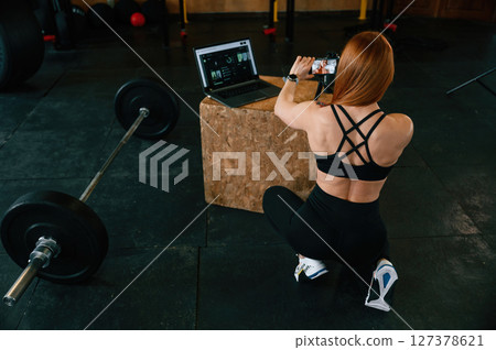 View from the back. Shooting video by smartphone. Beautiful strong woman is in the gym View from the back. Shooting video by smartphone. Beautiful strong woman is in the gym 127378621