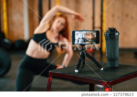 Shooting video by smartphone. Doing exercises. Beautiful strong woman is in the gym Shooting video by smartphone. Doing exercises. Beautiful strong woman is in the gym 127378623