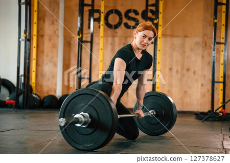 Leaning on the barbell. On the floor. Beautiful strong woman is in the gym 127378627