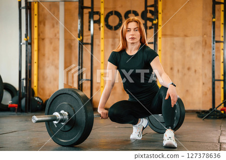 Front view. Sitting, barbell on the floor. Beautiful strong woman is in the gym 127378636
