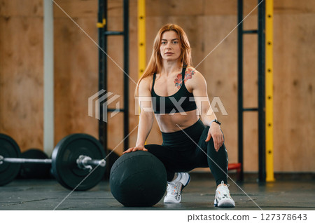 Front view. Sitting, barbell on the floor. Beautiful strong woman is in the gym Front view. Sitting, barbell on the floor. Beautiful strong woman is in the gym 127378643
