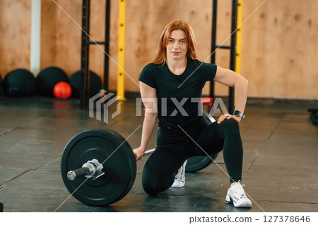 Sitting with barbell on the floor. Beautiful strong woman is in the gym 127378646