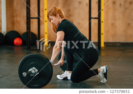 View from the side. Sitting with barbell on the floor. Beautiful strong woman is in the gym View from the side. Sitting with barbell on the floor. Beautiful strong woman is in the gym 127378651