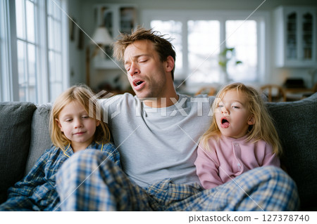 A man and two children are sitting on a couch, with the man looking tired 127378740