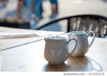 Two white cups of coffee on a table of outdoor cafe. 127381278
