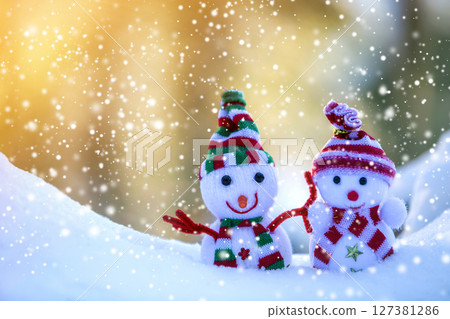 Two small funny toys baby snowman in knitted hats and scarves in deep snow outdoors on bright blue and white copy space background. Happy New Year and Merry Christmas greeting card. 127381286