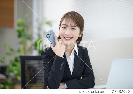 A young businesswoman working on a computer with a smartphone 127382090