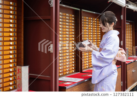 Young Japanese woman in traditional Japanese clothing drawing fortune at a shrine 127382111