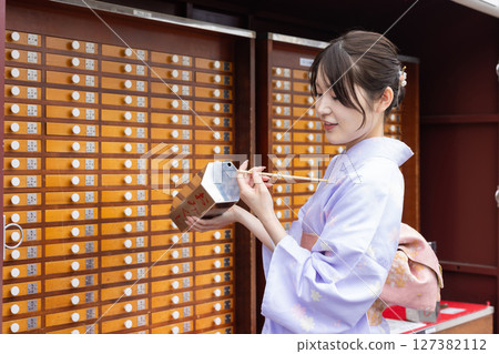 Young Japanese woman in traditional Japanese clothing drawing fortune at a shrine 127382112
