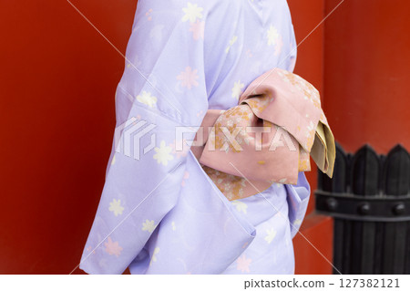A Japanese woman in traditional Japanese clothing standing in front of the vermilion wall of a shrine A Japanese woman in traditional Japanese clothing standing in front of the vermilion wall of a shrine 127382121
