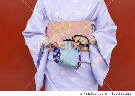 A Japanese woman in traditional Japanese clothing standing in front of the vermilion wall of a shrine A Japanese woman in traditional Japanese clothing standing in front of the vermilion wall of a shrine 127382125