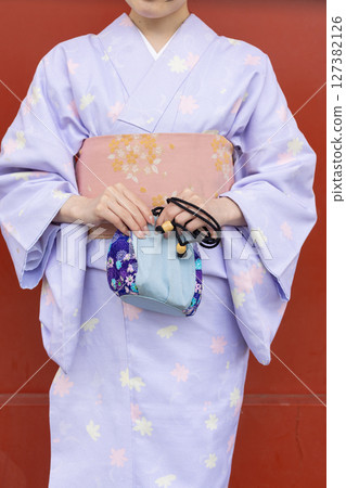 A Japanese woman in traditional Japanese clothing standing in front of the vermilion wall of a shrine A Japanese woman in traditional Japanese clothing standing in front of the vermilion wall of a shrine 127382126