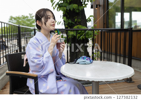 A young Japanese woman wearing a kimono sitting on a terrace at a cafe 127382132