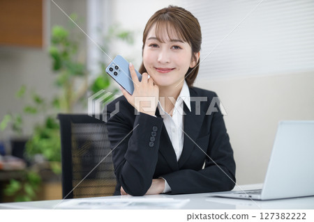 A young businesswoman working on a computer with a smartphone A young businesswoman working on a computer with a smartphone 127382222