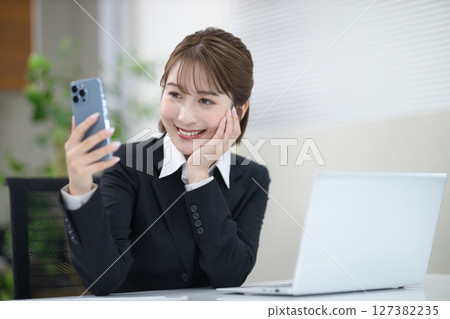 一位年輕的女商人正在做案頭工作，看著她的智慧型手機 127382235