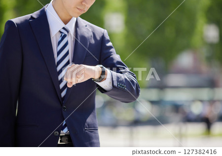 A young businessman in a suit looking at his watch in a business district 127382416