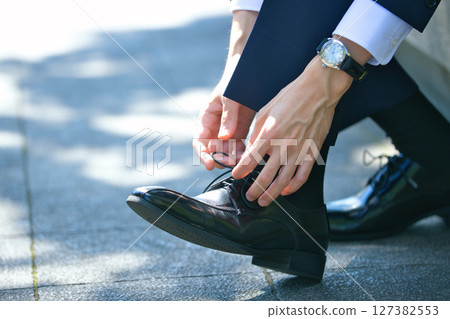 The feet of a young man in a suit tying the laces of his business shoes 127382553