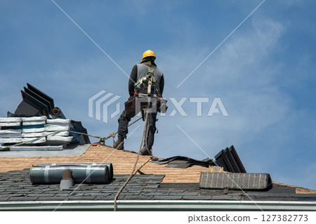 Professional Roofer with Hard Hat and Nailer Installing Shingles on Residential Roof 127382773
