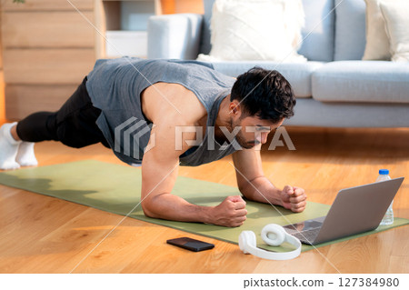 Young asian man doing plank exercise in living room at home while watching online workout tutorial. Young asian man doing plank exercise in living room at home while watching online workout tutorial. 127384980