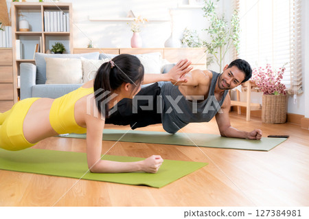 Young asian couple practicing workout with plank while high-five in living room at home. 127384981