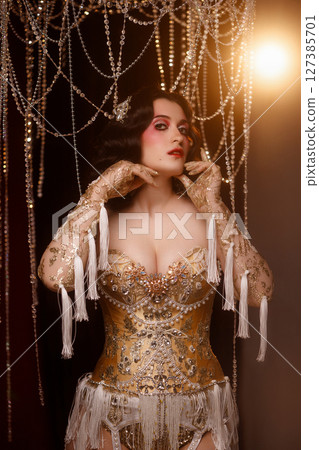 Cabaret dancer in vintage corset costume standing under chandelier on dark stage Cabaret dancer in vintage corset costume standing under chandelier on dark stage 127385701