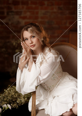 Woman in white dress sitting on chair in conceptual indoor swamp art setup 127385706