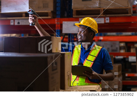 Man African American professional worker wearing safety uniform and white hard hat using bar code reader scanning box inspect product on shelves in warehouse. Man African American professional worker wearing safety uniform and white hard hat using bar code reader scanning box inspect product on shelves in warehouse. 127385902