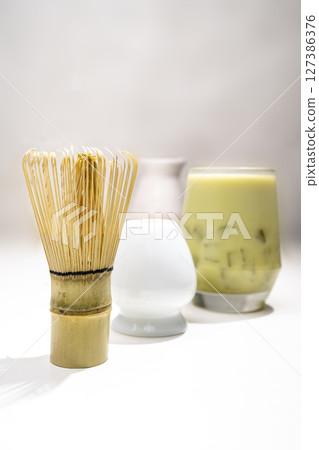 Closeup view of iced matcha green tea on the glass with a traditional bamboo brush whisk or chasen on the table. Accessories for making matcha green tea 127386376