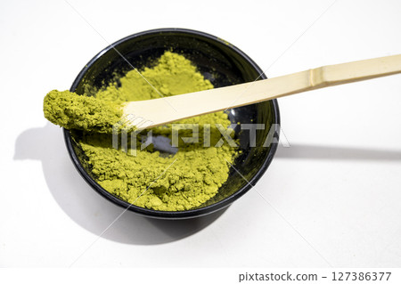 Matcha green tea powder in the black bowl and a traditional bamboo spoon or chashaku on a white background. Accessories for making matcha green tea 127386377