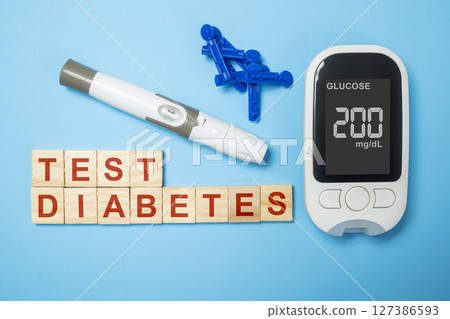 Glucometer with the glucose level on the screen with lancet and text of diabetes test on wooden cubes. Concept of diabetes or a healthy lifestyle Glucometer with the glucose level on the screen with lancet and text of diabetes test on wooden cubes. Concept of diabetes or a healthy lifestyle 127386593
