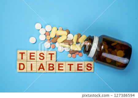 Pills from a container with the text of a diabetes test on wooden cubes. Concept of diabetes or a healthy lifestyle 127386594