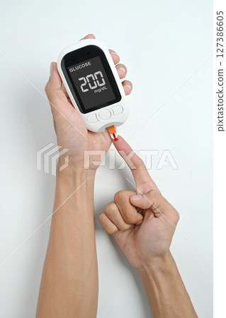 Human hand using a glucometer for checking blood sugar level isolated over a white background. Concept of diabetes or a healthy lifestyle 127386605