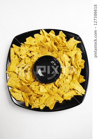 Nachos tortilla chips on the black plate with an empty bowl for sauce on a white background. Food and snacks concept 127386618