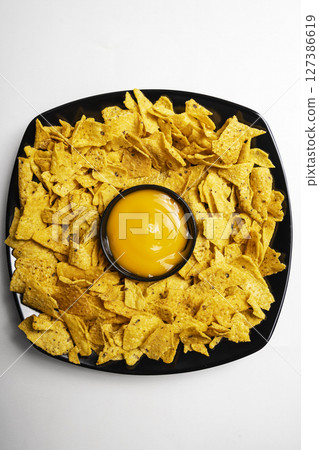 Nachos tortilla chips on the black plate with cheese sauce in a bowl on a white background. Food and snacks concept Nachos tortilla chips on the black plate with cheese sauce in a bowl on a white background. Food and snacks concept 127386619