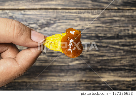 Human hand holding a nachos tortilla chip with salsa barbecue sauce on the table. Food and snacks concept Human hand holding a nachos tortilla chip with salsa barbecue sauce on the table. Food and snacks concept 127386638
